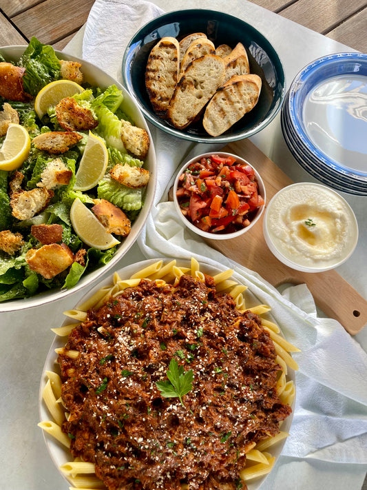 Braised Beef Bolognese with Penne, Toasted Crostini, Caesar Salad, Whipped Ricotta, and Bruschetta